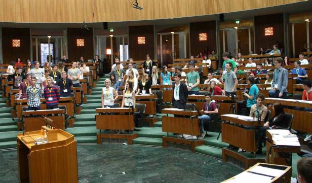 Eine Gruppe junger Menschen sitzt oder steht in einem großen Sitzungssaal.