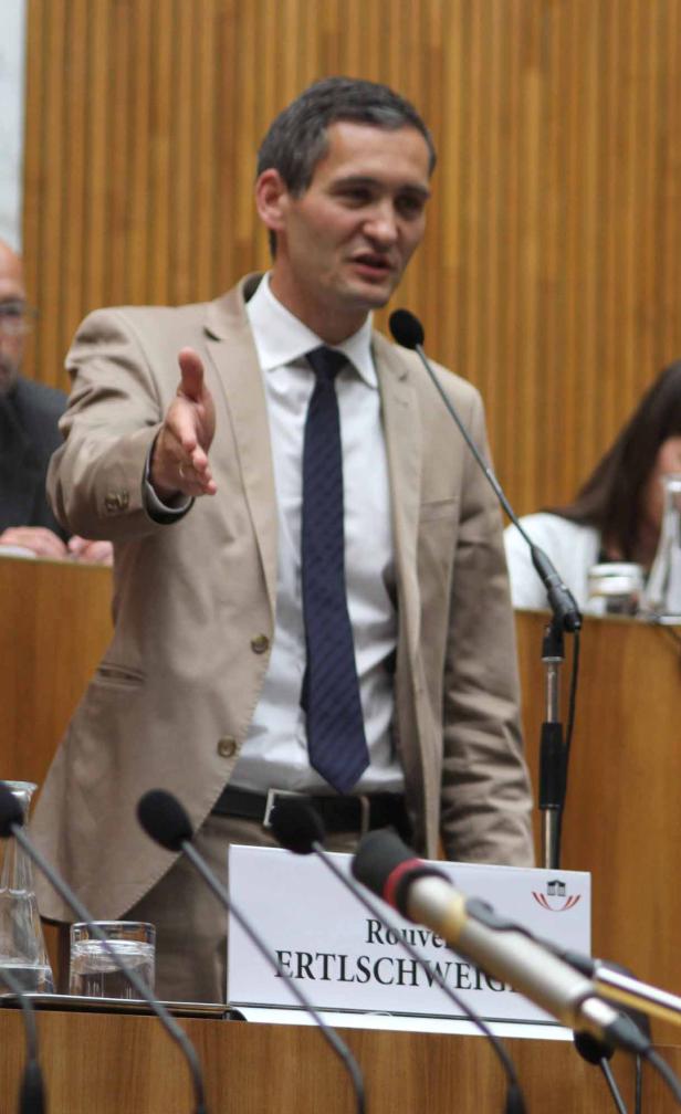 Rouven Ertlschweig gestikuliert während einer Rede vor Mikrofonen.