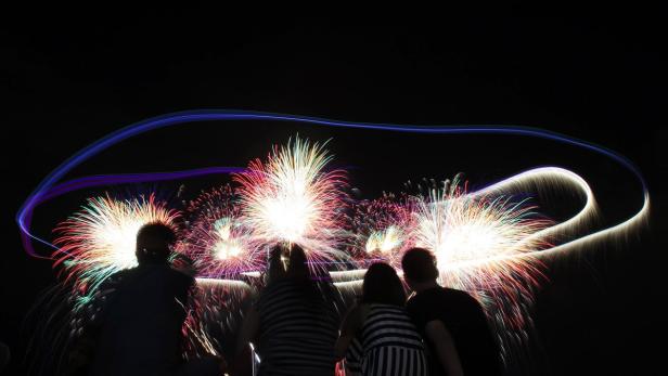 Eine Gruppe von Menschen beobachtet ein farbenfrohes Feuerwerk am Nachthimmel.