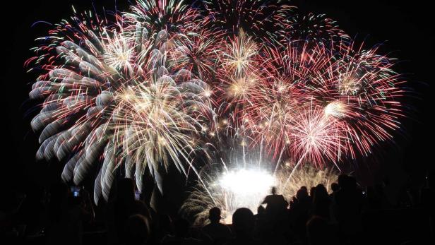 Eine Menschenmenge beobachtet ein farbenfrohes Feuerwerk am Nachthimmel.