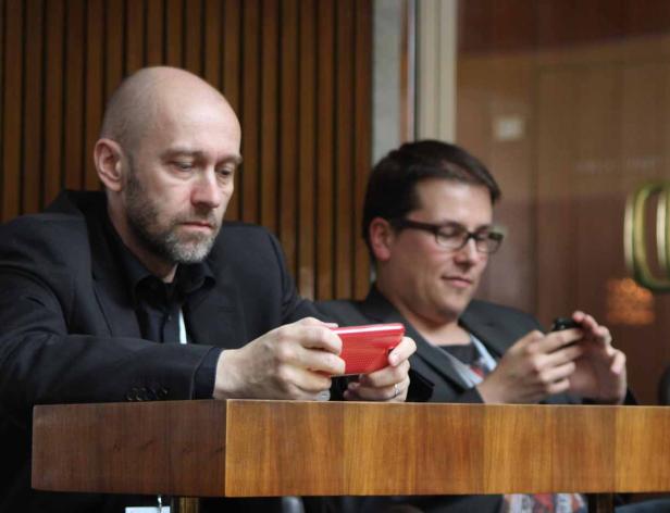 Zwei Männer sitzen an einem Tisch und schauen auf ihre Smartphones.