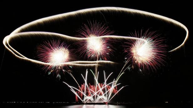 Ein Feuerwerk erhellt den Nachthimmel mit roten und weißen Lichtern und geschwungenen Bahnen.