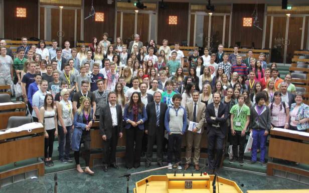 Eine große Gruppe von Menschen steht in einem Raum mit Holzvertäfelung.
