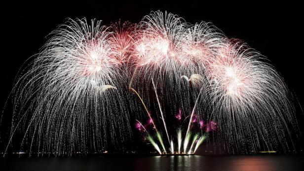 Mehrfarbiges Feuerwerk erhellt den Nachthimmel über dem Wasser.