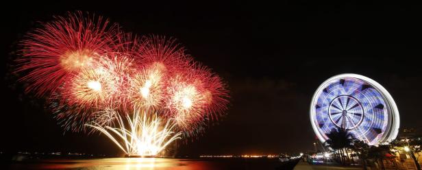 Ein Feuerwerk erhellt den Nachthimmel neben einem beleuchteten Riesenrad.