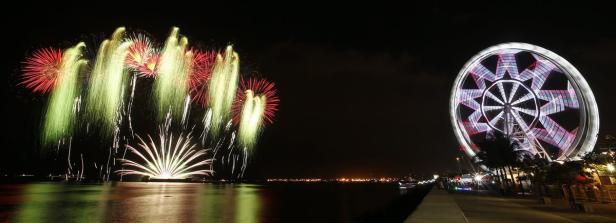 Ein beleuchtetes Riesenrad und ein Feuerwerk erhellen den Nachthimmel über dem Wasser.