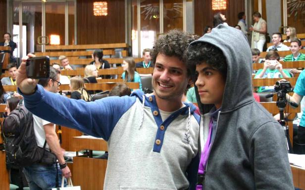 Zwei junge Männer machen ein Selfie in einem Hörsaal mit Publikum.