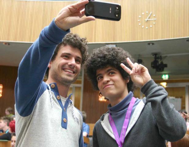 Zwei junge Männer machen ein Selfie in einem Auditorium.