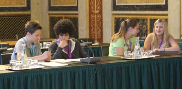 Vier junge Leute sitzen an einem Tisch mit Mikrofonen und Wasserflaschen.