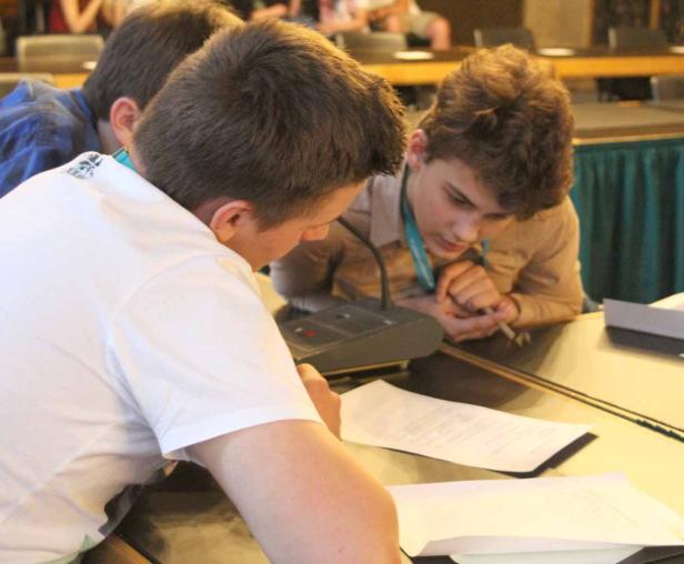 Drei junge Leute sitzen an einem Tisch und arbeiten an Dokumenten.