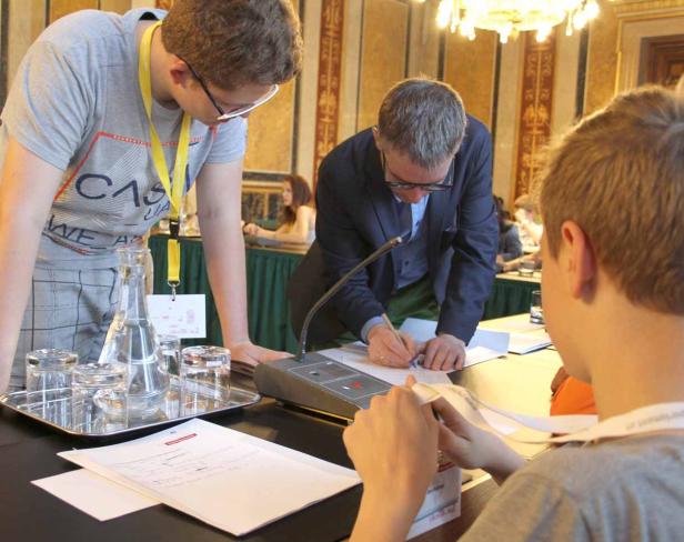 Mehrere Personen sitzen an einem Tisch und arbeiten an Dokumenten während einer Konferenz.