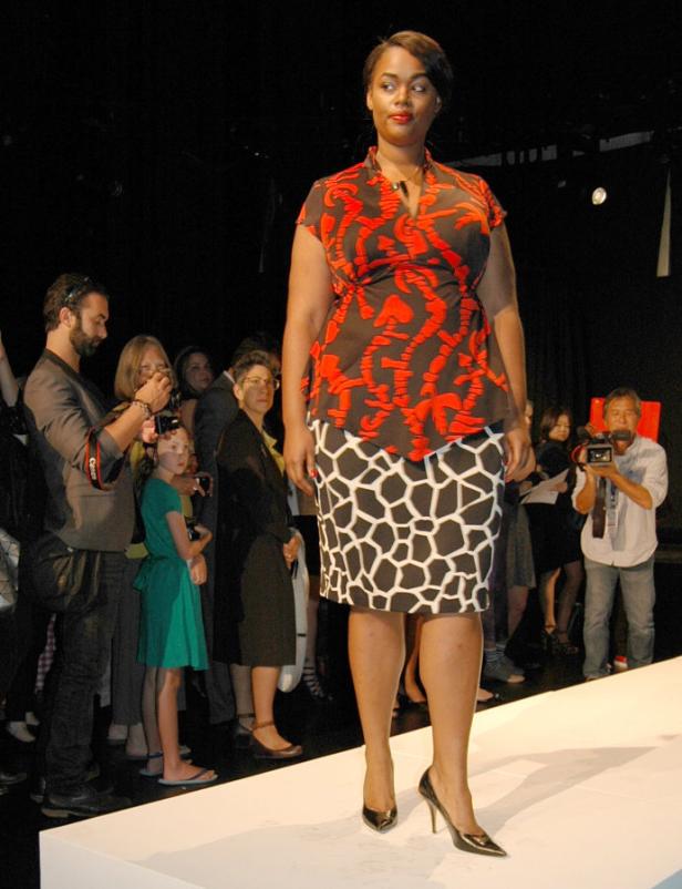 Eine Frau präsentiert Mode auf einem Laufsteg vor Publikum.