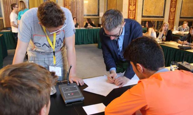 Mehrere Personen sitzen an einem Tisch und unterzeichnen ein Dokument.