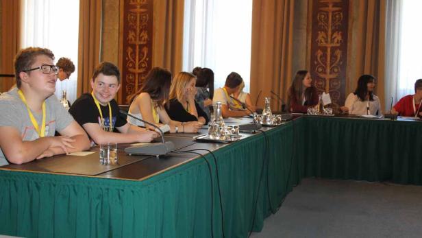 Eine Gruppe junger Leute sitzt an einem langen Tisch mit Mikrofonen.