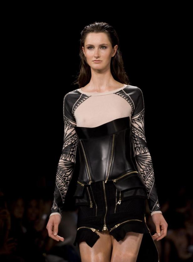 Eine Frau auf dem Laufsteg trägt ein schwarzes Korsett und einen Rock mit Reißverschlüssen.