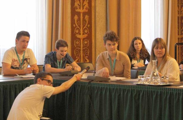 Eine Gruppe junger Leute sitzt an einem Tisch während einer Konferenz oder Diskussion.