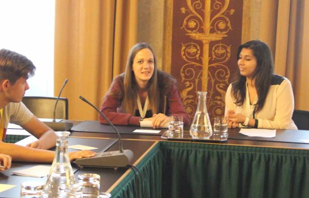 Drei Personen sitzen an einem Tisch mit Mikrofonen bei einer Konferenz.