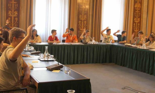 Eine Gruppe junger Leute sitzt an einem Tisch und hebt die Hände.