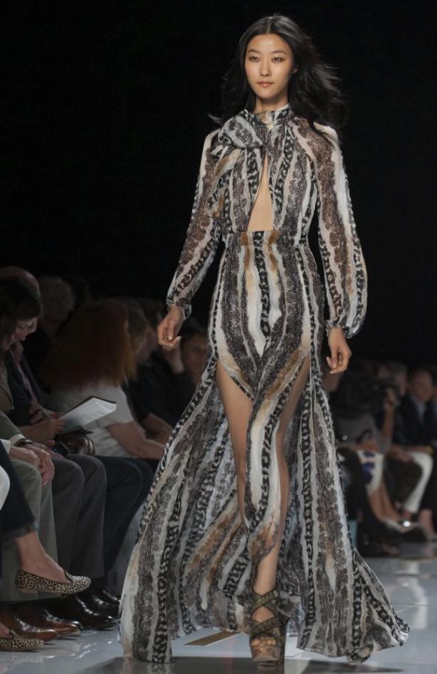 Eine asiatische Frau präsentiert ein langes, gemustertes Kleid mit Beinschlitz auf einem Laufsteg.