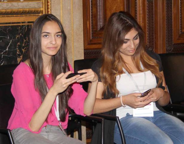 Zwei junge Frauen sitzen nebeneinander und benutzen ihre Smartphones.