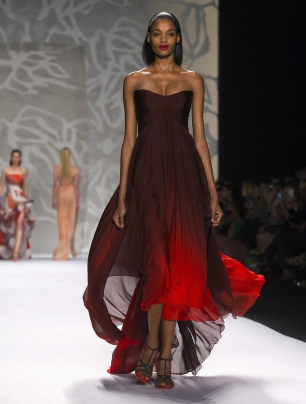 Eine Frau in einem trägerlosen, weinroten Kleid mit Farbverlauf läuft über einen Laufsteg.