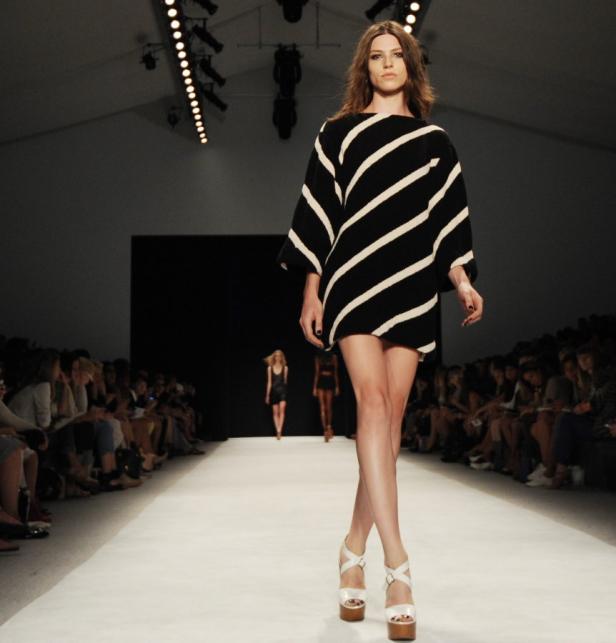 Eine Frau in einem schwarz-weiß gestreiften Kleid läuft auf einem Laufsteg.