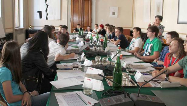 Eine Gruppe junger Leute sitzt an einem langen Tisch bei einer Konferenz.