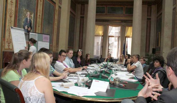 Eine Gruppe junger Leute sitzt an einem ovalen Tisch in einem Konferenzraum.