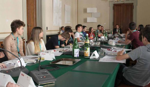 Eine Gruppe junger Leute sitzt an einem langen Tisch bei einer Konferenz.