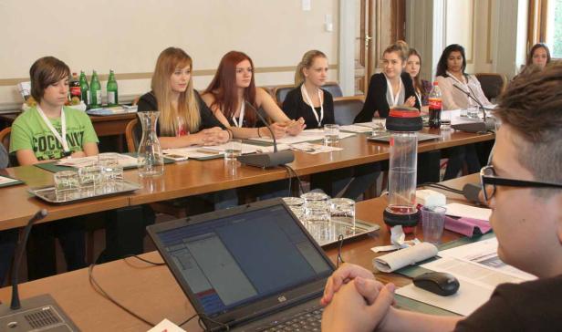 Eine Gruppe junger Leute sitzt an einem langen Tisch bei einer Konferenz oder einem Seminar.