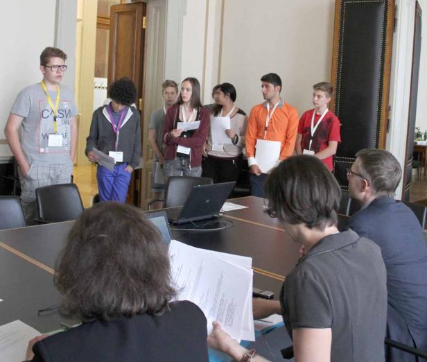 Eine Gruppe Jugendlicher steht in einem Raum und hält Papiere in der Hand.