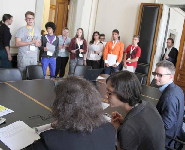 Eine Gruppe junger Leute steht in einem Konferenzraum hinter einem Tisch.