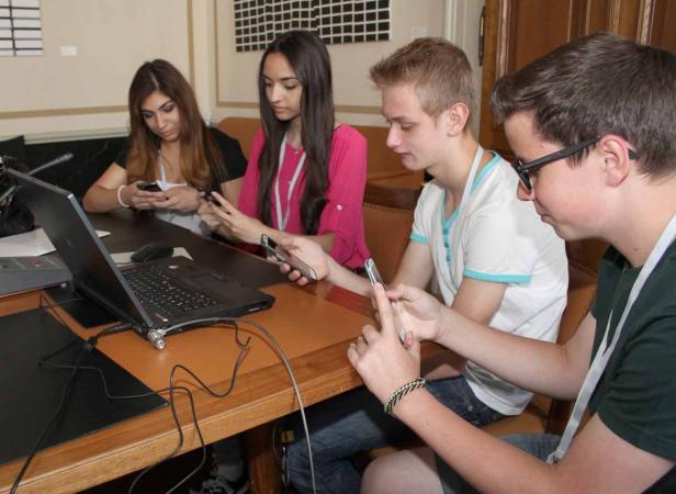 Vier junge Leute sitzen an einem Tisch und benutzen ihre Smartphones.