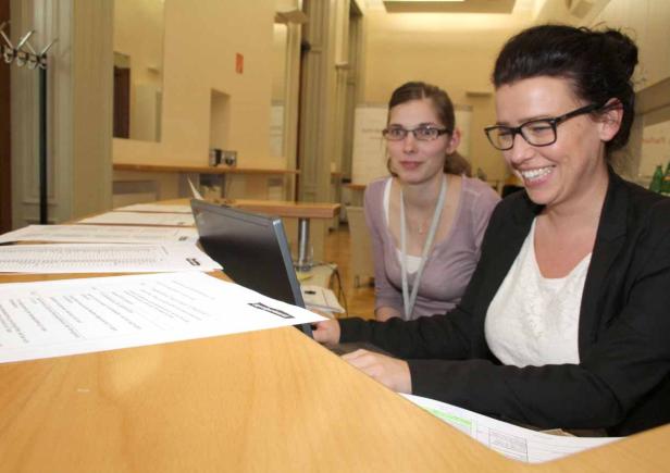 Zwei Frauen sitzen an einem Tisch mit einem Laptop und Dokumenten.