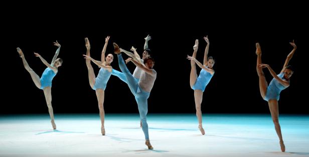 Eine Gruppe von Balletttänzern und -tänzerinnen führt eine synchrone Choreografie auf einer Bühne auf.