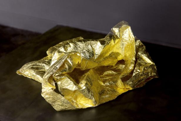 Ein zerknülltes Stück Goldfolie liegt auf einer dunklen Oberfläche.