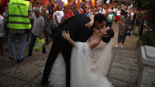 Ein Brautpaar küsst sich vor einer Menschenmenge mit Flaggen.