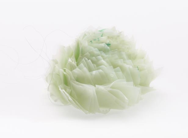 Eine Blume aus transparenten, hellgrünen Kunststoffstücken auf weißem Grund.