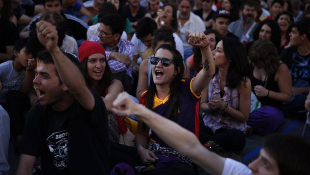 Eine Menschenmenge sitzt und jubelt mit erhobenen Fäusten.