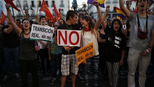 Eine Menschenmenge demonstriert mit Schildern, die „Transición real, sin rey“ und „NO“ zeigen.