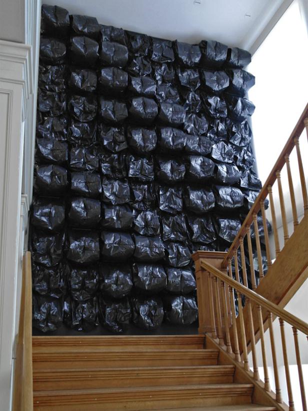 Eine Wand ist mit vielen schwarzen Müllsäcken dekoriert, neben einer Holztreppe.