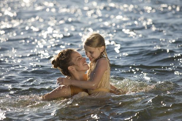 Eine Frau und ein Mädchen umarmen sich im glitzernden Wasser.