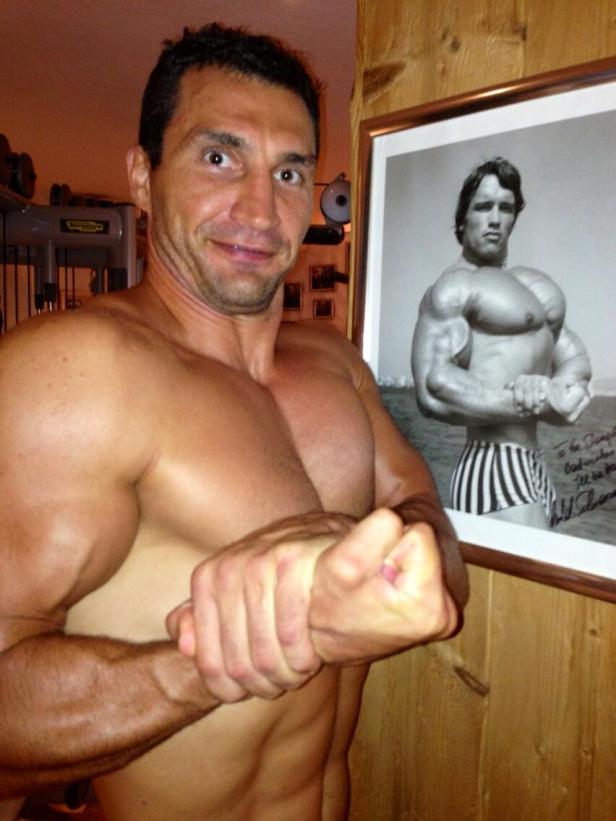 Ein muskulöser Mann posiert vor einem gerahmten Foto von Arnold Schwarzenegger.