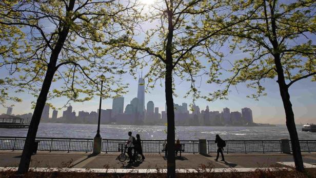 Menschen spazieren am Ufer mit Blick auf die Skyline von New York City.