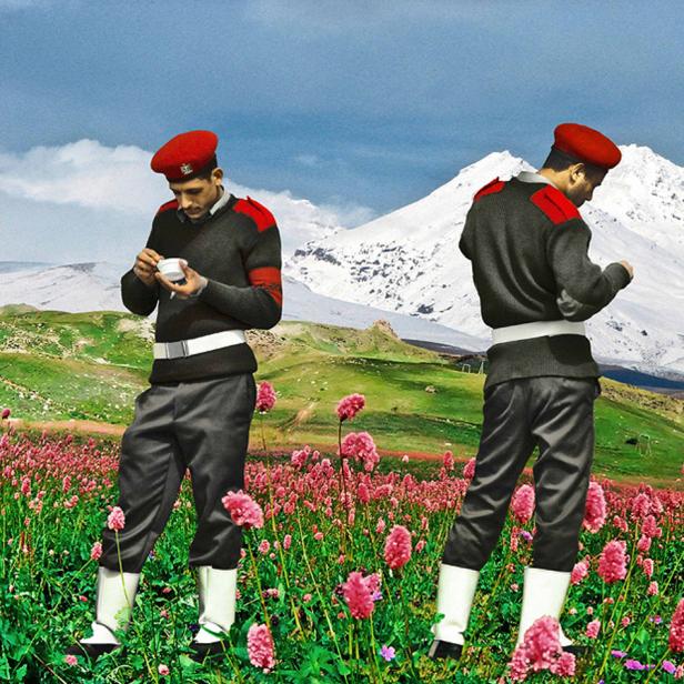 Zwei Männer in Uniform stehen auf einer Blumenwiese vor einem Bergpanorama.