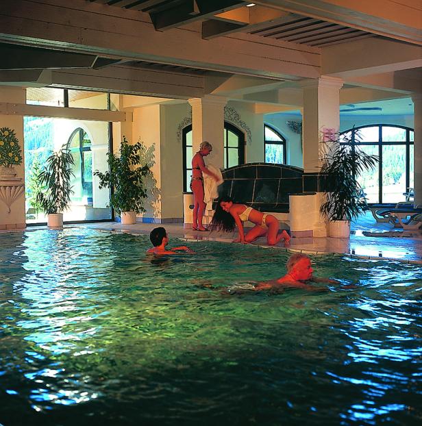 Mehrere Personen entspannen sich in einem Hallenbad mit großen Fenstern.