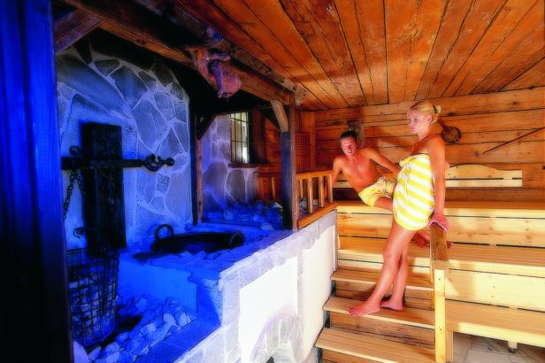 Ein Mann und eine Frau in Handtüchern in einer traditionellen Holzsauna.