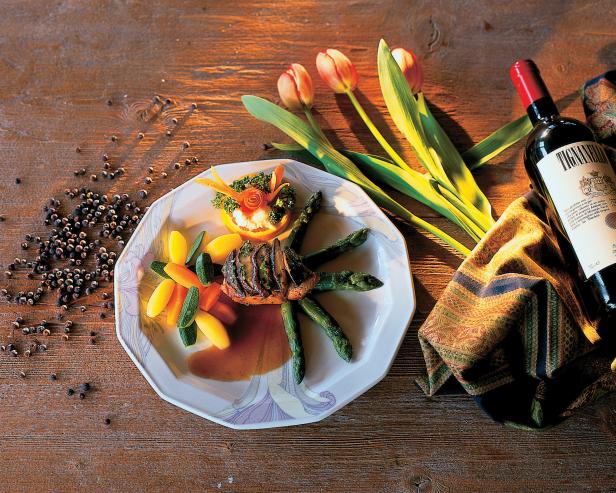 Ein Teller mit einem Fleischgericht, Spargel, Gemüse und einer Flasche Tignanello-Wein auf einem Holztisch.
