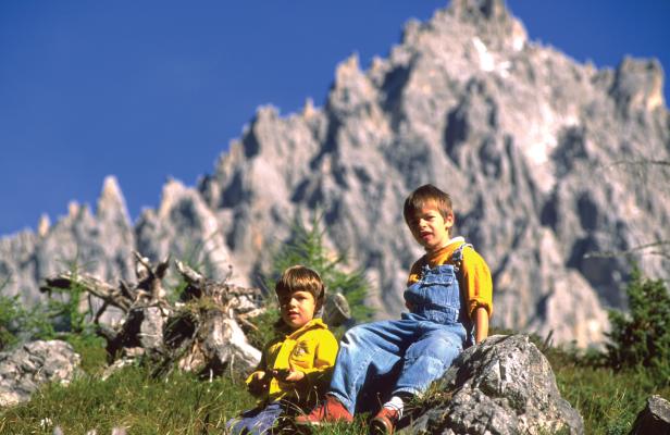 Zwei Jungen sitzen vor einer Bergkulisse im Gras.