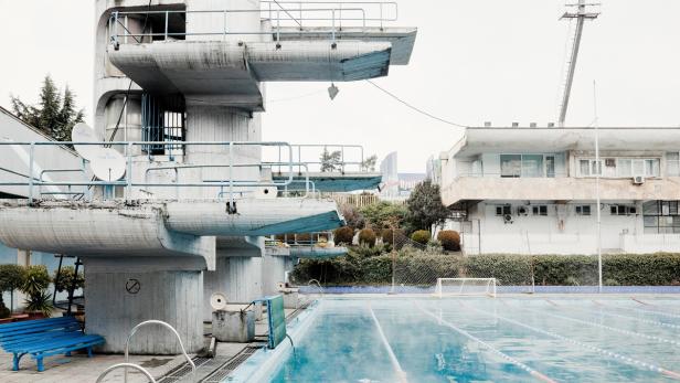 Ein Schwimmbad mit Sprungturm und einem blauen Becken im Vordergrund.